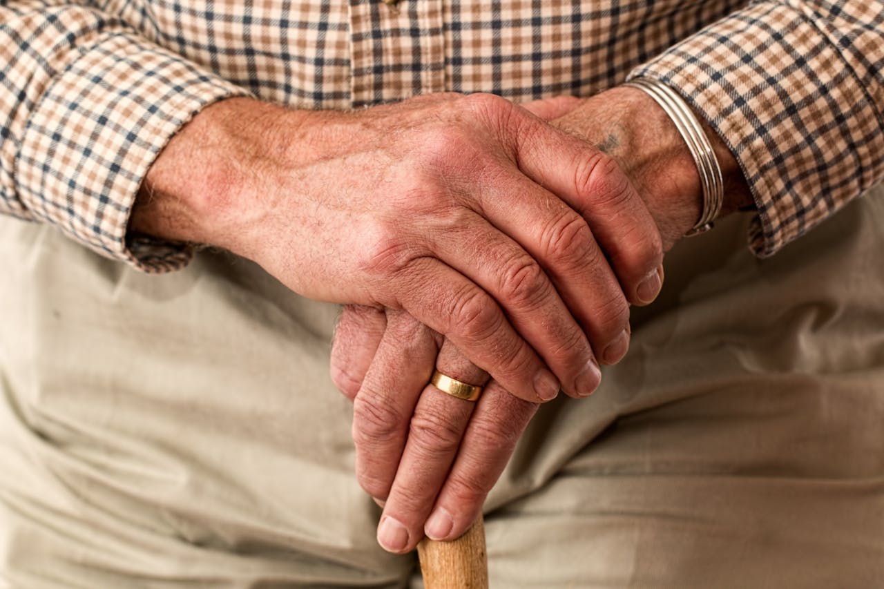 A detailed image of elderly hands clasping a wooden cane, symbolizing aging and support.