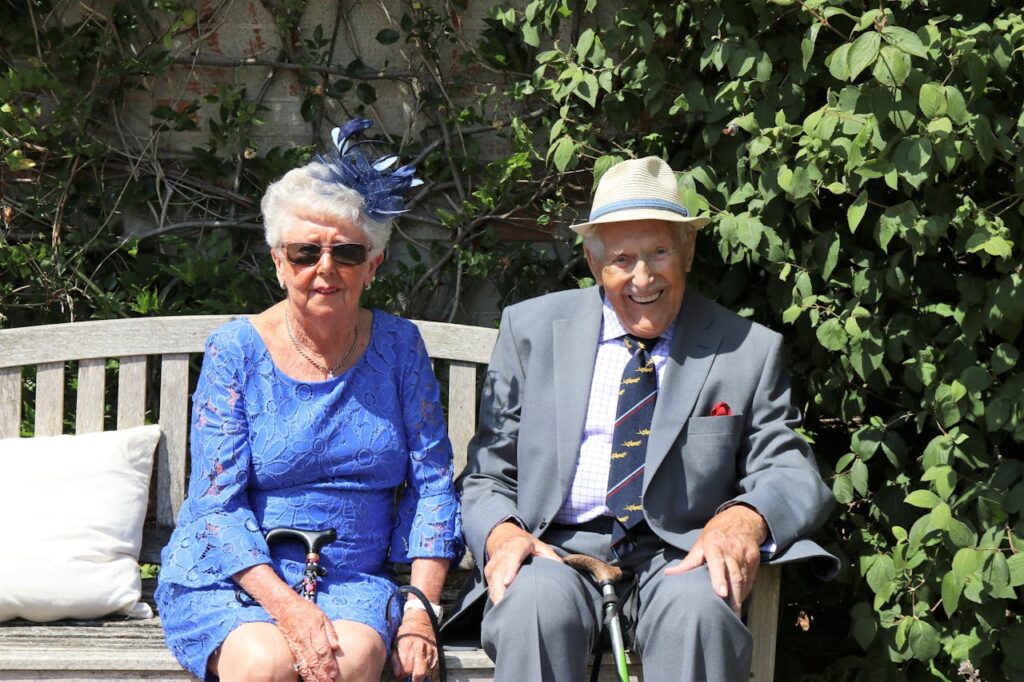 A happy elderly couple sitting together on a garden bench, smiling outdoors.