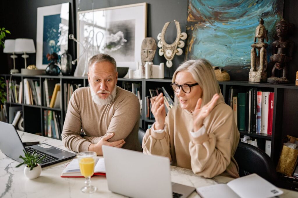 Senior couple enjoys online learning in a cozy home setting with laptops and books.