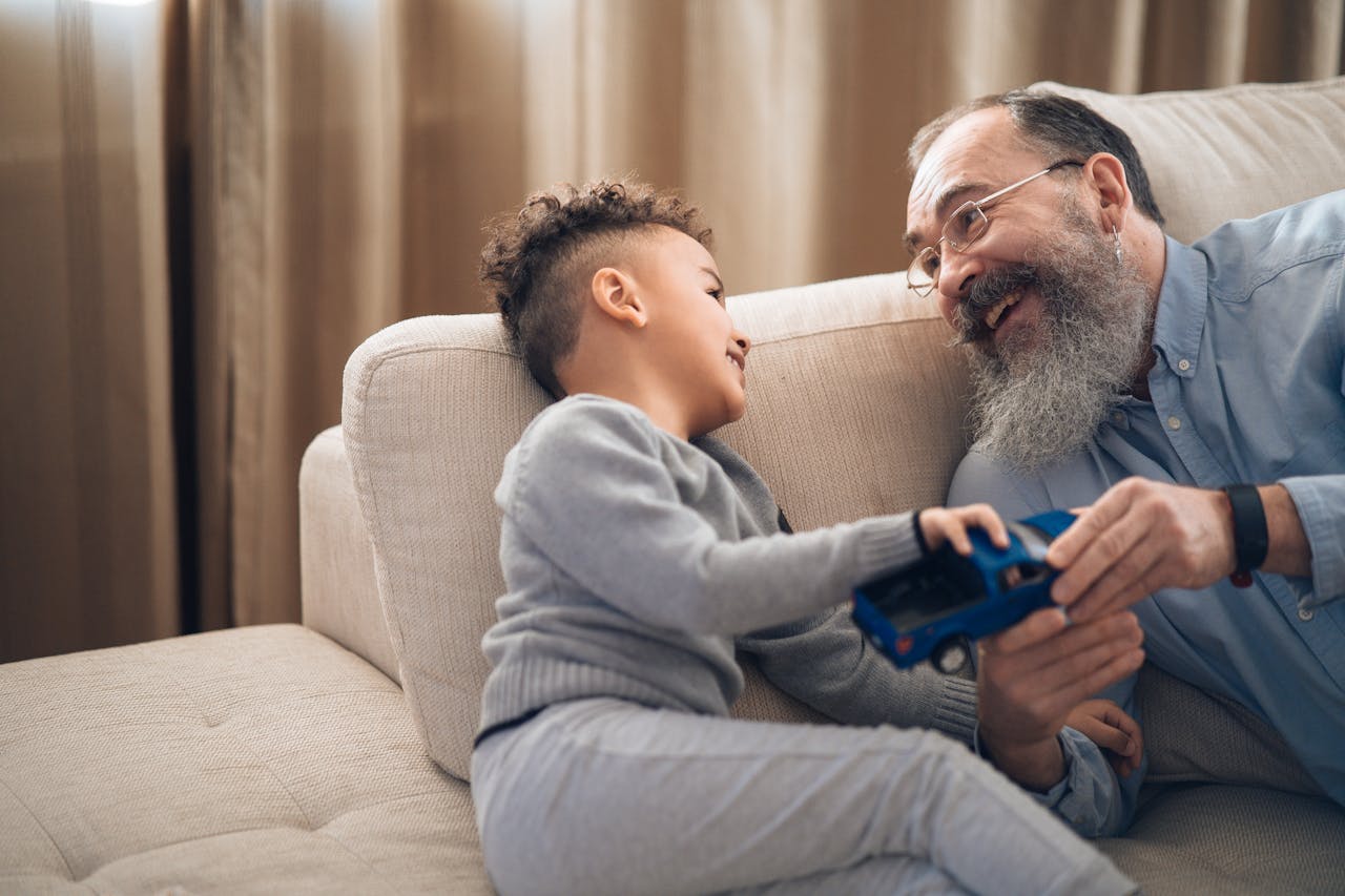 A joyful grandfather and grandson sharing a playful moment on the couch, indoors.