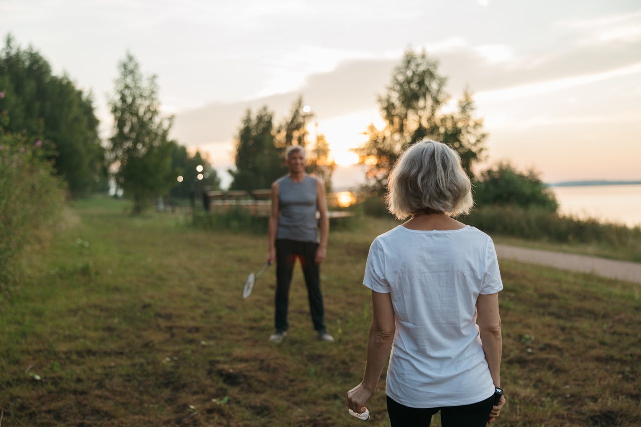 Elderly couple playing badminton outdoors at sunset, enjoying leisure time together.